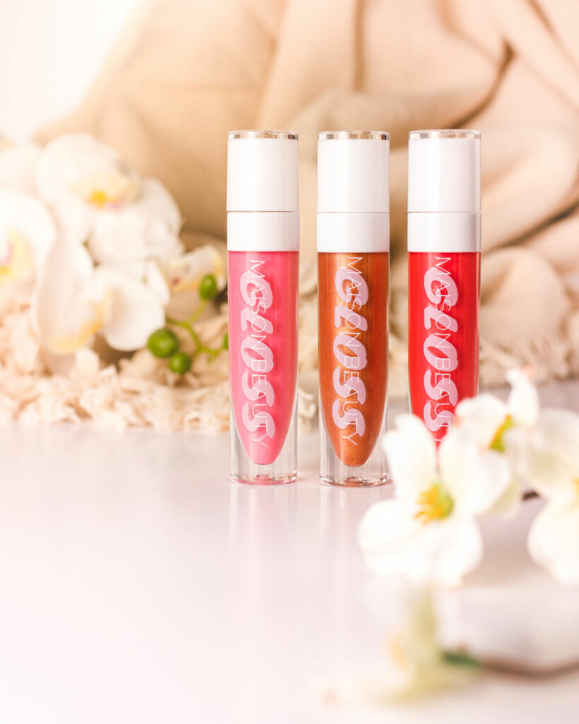 set of pink, brown and red lipgloss in line surrounded with white flowers