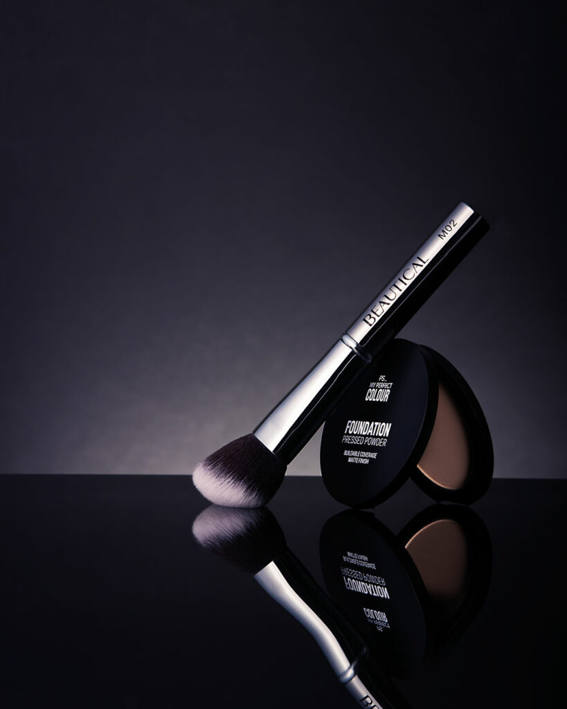 face brush and cosmetic touching together on a black reflected surface
